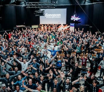 A crowd of people standing with arms open, with the Django poney and DjangoCon Europe 2019 logo in the background